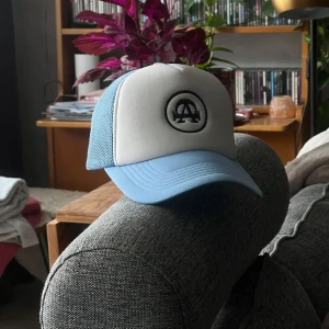 Blå och vit keps från Alla Cap 1 - Snygg keps i blått och vitt från Alla Cap med svart broderad logga framtill. Kepsen har mesh på sidorna och bak, samt böjd skärm. Perfekt för dig som vill ha en stilren look. Kepsen har aldrig varit använd det är därför den säljs. 