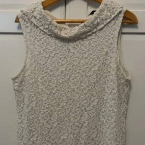 Vit spetsärmlös topp från Stockh LM - Säljer en vit ärmlös topp från Stockh LM med vacker spets och krage. Perfekt för dig som vill ha en romantisk och stilren look. Toppen har ett blommigt spetsmönster och är fodrad för extra komfort.