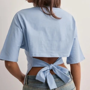 Ljusblå topp med knyt i ryggen - Säljer en ljusblå topp med korta ärmar och snygg knytning i ryggen. Toppen har en croppad passform och är tillverkad i mjuk bomull. Perfekt för vår och sommar!