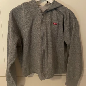 Grå zip hoodie från Levi's - Säljer en klassisk grå hoodie från Levi's med dragkedja framtill och liten röd logotyp på bröstet.
