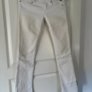 Vita jeansbyxor från Replay - Snygga vita jeansbyxor från Replay med klassisk femficksdesign och raka ben. Byxorna har diskreta sömmar och en liten röd Replay-detalj på bakfickan. Perfekta för en fräsch och stilren look.