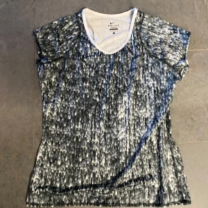 Nike Dri-Fit mönstrad t-shirt - Säljer en Nike Dri-Fit t-shirt med unikt svartvitt mönster. T-shirten har korta ärmar och är tillverkad i ett syntetmaterial som andas, perfekt för träning. Klassisk passform och rund halsringning.Stl L. 