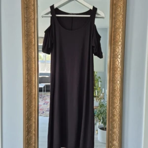 Svart axelbandslös klänning med volangärm - Svart klänning med axelbandslös design och korta volangärmar. Klänningen har en rak passform och är tillverkad i ett mjukt, stretchigt material.