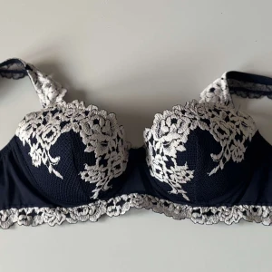 Intimissmi bh - Snygg marinblå  bh med vit spetsdetalj över kuporna och längs kanten. Bh:n har vackert blommönster i spetsen och justerbara axelband. Perfekt för dig som vill ha något extra fint under kläderna. Produkten är aldrig använd därför är den i mycket bra skick. 🫶🏻☺️