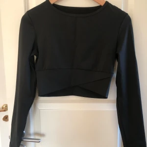 Svart croppad långärmad sporttopp - Snygg svart croppad sporttopp med långa ärmar och rund halsringning. Toppen har en stilren design med en lätt omlott-effekt framtill. Är i vanligt tröningsmaterial i passform xs 🖤