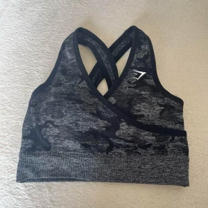 Svart och grå sport-bh från Gymshark  - Säljer en svart och grå sport-bh från Gymshark med camouflagemönster och korsade axelband i ryggen. Perfekt för träning och har en tight passform som ger bra stöd. Gymshark camo top, mycket fint skick. Populär model som inte säljs  längre! Storlek: xs  Kika gärna in på mina andra annonser, säljer fler träningskläder  och kan samfrakta!