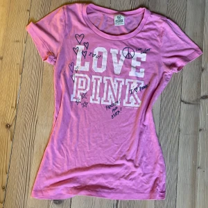 Rosa t-shirt från Victoria's Secret PINK - Säljer en rosa t-shirt från Victoria's Secret PINK med tryck 'LOVE PINK' och handritade hjärtan och stjärnor på framsidan. T-shirten har rund halsringning och korta ärmar. Perfekt för en färgglad och avslappnad stil!