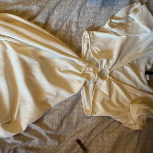 Ljusvit långklänning med ringdetalj - Supersnygg långklänning i ljusvit nyans med cool ringdetalj framtill som samlar tyget. Klänningen har korta ärmar och en mjuk, stretchig känsla. Perfekt för dig som vill sticka ut med en trendig och stilren look.