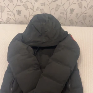 Svart dunjacka från Canada Goose M - Säljer en svart dunjacka från Canada Goose i storlek M. Jackan har huva, dragkedja och är riktigt tjock och varm. Perfekt för kalla vinterdagar och har klassisk Canada Goose-logga på insidan. Fylld med dun och fjädrar för maxad värme.