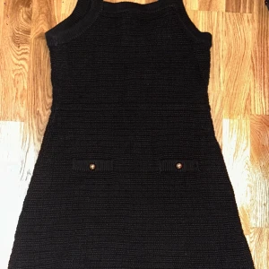 Svart stickad klänning från H&M - Svart stickad klänning från H&M i storlek L. Ärmlös modell med rund halsringning och två små fickor framtill med dekorativa knappar. Tjockt stickat material som ger en cool och enkel look.