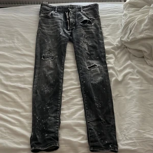 Svarta jeans från Dsquared2 - Riktigt snygga svarta jeans från Dsquared2 med slitningar, dragkedjedetalj och coolt stänkmönster. Jeansen har låg midja och är tillverkade i bomull med en touch av stretch för skön passform. Perfekta för dig som gillar en edgy streetstil. Nypris 16800, mitt pris 3995. Hör av er vid intresse!