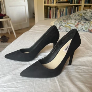 Svarta pumps med spetsig tå - Stilrena svarta pumps i mocka-look med spetsig tå och hög klack från Nelly. Bra skick.