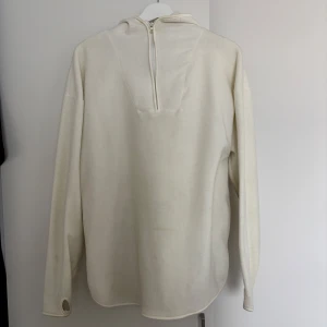 Vit fleecehoodie med half zip - Mysig vit hoodie i fleece med huva och half zip framtill. Tröjan har långa ärmar med tumhål och en avslappnad passform. Perfekt för kyliga dagar när du vill vara både bekväm och stilren.