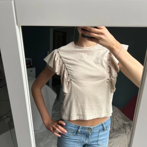 Beige volangtopp - Snygg beige topp med volangdetaljer längs axlarna och små kulor som dekoration. Perfekt för dig som gillar unika detaljer och en chill vibe, använd 3 gånger. Storlek 158 från Zara men passar XS-S, jag har S i vanliga fall 