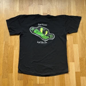 Gato Loco Svart T-Shirt - Gato Loco T-Shirt med tryck både fram och bak i färgen Svart. OBS! Sömnen har gått upp lite i nacken! Storlek: L (Ingen lapp men uppskattar), Armhåla till Armhåla: 56 cm, Längd: 70 cm, Axel till Armöppning: 19 cm.  Material: Ingen lapp men skulle säga 100% bomull. 