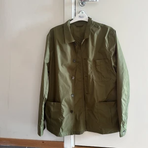 Olivgrön overshirt från Stenströms - Snygg olivgrön overshirt från Stenströms med klassisk krage och knäppning framtill. Jackan har tre stora fickor och är tillverkad i ett lätt syntetmaterial, perfekt för lager-på-lager. Enkel och clean design som funkar till många stilar.