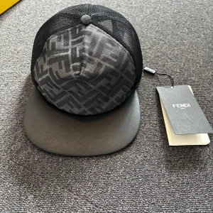 Svart Fendi keps  - Snygg svart keps från Fendi med FF-mönster framtill och mesh-bakstycke för extra ventilation. Justerbar passform baktill med gulddetalj. Kepsen levereras med originalkartong och dustbag. Skriv till mig för fler frågor:)