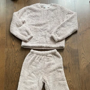 Beige fluffigt sett från H&M - Supermjuk och fluffigt beige sett från H&M i storlek 146/152. Tröjan har lång ärm, rund hals och är gjord i ett gosigt fleecematerial som är perfekt för kyliga dagar. Byxorna är också i ett gosigt fleecemsterial. Enkel och stilren design som är lätt att matcha. 