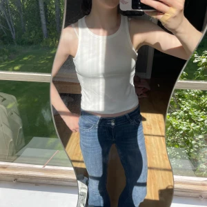 Vit ribbad linnetopp från H&M - Säljer en vit ribbad linnetopp från H&M med klassisk rund halsringning och croppad passform. Perfekt för varma dagar och enkel att styla med jeans eller kjol. Materialet är mjukt och stretchigt för en bekväm känsla.