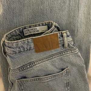 Ljusblå jeans från Vero Moda - Säljer ett par ljusblå jeans från Vero Moda med klassisk femficksdesign och snyggt läderpatch bak. Jeansen är mid waist och är tillverkade i slitstarkt denim. Perfekta till sneakers eller boots.