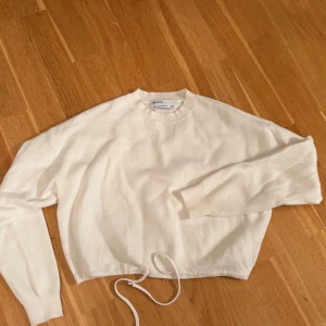Vit croppad tröja från Bershka - Säljer en vit croppad tröja från Bershka med rund hals och långa ärmar. Tröjan har snörning nertill för en snygg passform och är gjord i mjukt material. Perfekt för dig som gillar enkel och stilren look.