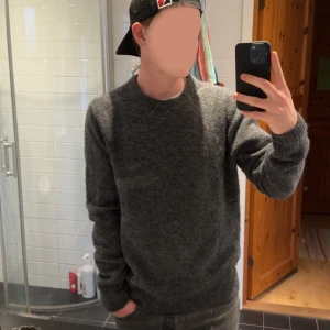 Mörkgrå tröja - Mysig mörkgrå stickad tröja med rund halsringning och långa ärmar. Perfekt för kyliga dagar och enkel att matcha med jeans eller andra byxor. Klassisk modell med ribbade muddar vid ärmslut och nederkant.