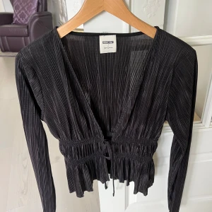 Svart plisserad blus från ABOUT YOU - Supersnygg svart plisserad blus/ kofta från ABOUT YOU x Lena Gercke. Blusen har djup v-ringning, volang nertill och knyt i midjan. Pris kan alltid diskuteras 