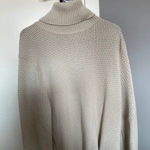 Beige stickad polotröja - Snygg beige stickad polotröja med hög krage och långärmad modell. Tröjan har ett diskret rutmönster i stickningen och är perfekt för lager-på-lager under kyliga dagar.används bara en gång