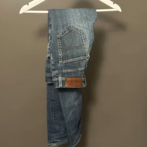 Tiger of Sweden Evolve jeans blå 28/32 - Snygga blå jeans från Tiger of Sweden, modell Evolve. Jeansen har en klassisk femficksdesign, smal passform och normal midja. Tillverkade i Italien i ett mjukt och slitstarkt denimtyg. Perfekta för dig som gillar en stilren och modern look.