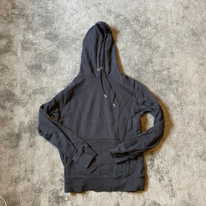 Svart hoodie från Lager 157 i bomull - Svart hoodie från Lager 157 i 100% bomull. Klassisk modell med huva och snörning, samt stor känguruficka framtill. Långärmad och mjuk insida, perfekt för chill dagar. Enkel och stilren design som funkar till det mesta.