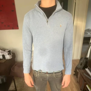 Ljusblå half zip tröja från Ralph Lauren - Snygg ljusblå långärmad tröja från Ralph Lauren med half zip och klassisk broderad logga på bröstet. Tröjan är i mjuk bomull och har en stilren, normal passform. Perfekt för dig som gillar en clean och avslappnad look. Storlek Xl i barnstorlek/ S