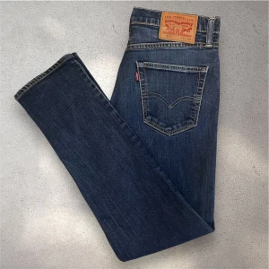 mörkblå Levi’s 511 jeans - Säljer ett par Levi's 511 jeans i mörkblå tvätt. Modellen är slim och har klassisk femficksdesign, med snygga kontrastsömmar och läderpatch bak. Personen på bilden är 180 cm och väger 63kg. Skicket är perfekt, skriv vid frågor!