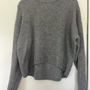 Grå stickad tröja från H&M - Mysig grå stickad tröja från H&M i storlek XS. Tröjan har en enkel design med lång ärm och ribbade detaljer vid nederkant och ärmslut. Tröjan är i storlek xs och sitter väldigt fint på, jag säljer den för att jag har alldeles för många gråa tröjor, den jar tyvärr blivit lite nopprig!