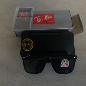 Svarta Ray-Ban Wayfarer solglasögon - Snygga svarta Ray-Ban Wayfarer solglasögon med polariserade glas. Klassisk fyrkantig form och diskret logga på linsen. Kommer med originalfodral, putsduk och box. Perfekta för att ge din stil en cool edge i solen.
