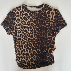 Leopardmönstrad topp med rynkdetalj - Cool topp med leopardmönster i bruna och svarta toner. Modellen har korta ärmar och en snygg rynkdetalj på sidan som ger en trendig look. Toppen är aldrig använd