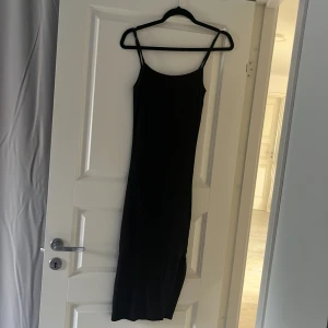 Svart ribbad långklänning med slits - Säljer en svart långklänning med smala axelband och ribbad struktur. Klänningen har en slits på sidan som ger en snygg detalj och är figurnära i modellen. Perfekt för dig som gillar minimalistisk och stilren look.