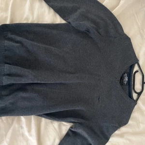 Grå bomullströja från Hampton Republic - Mörkgrå tröja från Hampton Republic i mjuk bomull. Klassisk v-ringning och diskret broderad logga på bröstet. Perfekt basic med ribbade muddar vid ärmslut och nederkant. Enkel att matcha med jeans eller chinos.