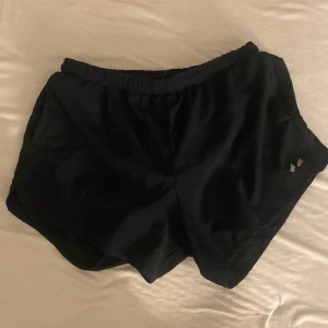 Svarta träningsshorts med resår - Svarta träningsshorts med elastisk midja och kort passform. Lätta och smidiga, perfekta för löpning eller gym. Materialet känns svalt och snabbtorkande. Diskret reflexdetalj på ena benet för extra synlighet. Aldrig använda 