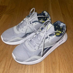 Sneakers - Snygga grå sneakers från Reebok med FuelFoam-sula för extra komfort. Ovandelen är i mesh och syntet, med vita och mörkblå detaljer samt coolt mönstrat foder i blått och gult. Perfekta för dig som gillar sportig stil och vill ha bekväma skor till träning eller vardag. Har några skador på tyget i skorna (inget som är synligt eller obekvämt) skorna är jättebekväma.