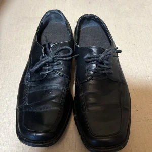 Svarta klassiska skinnskor med snörning - Stilrena svarta skinnskor med fyrkantig tå och snörning. Skorna har en platt sula och diskreta sömmar som ger en clean look. Perfekta för dig som gillar en klassisk och tidlös stil.