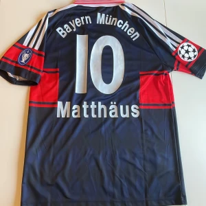 Bayern München Matthäus 10 Adidas tröja - Retro Bayern München replika fotbollströja med nummer 10 och Matthäus på ryggen. Adidas, med klassiska röda och mörkblå ränder, Champions League-patch på ärmen och Opel som sponsor. Vit krage med röda detaljer, klubbmärke på bröstet. Tillverkad i polyester. Endast handtvätt!