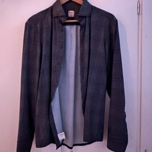 Grå rutig skjorta från Stenströms - Snygg grå skjorta från Stenströms i slimline-modell. Skjortan har ett klassiskt rutmönster i svart och vitt, långa ärmar och knäppning framtill. Perfekt för dig som gillar stilrena och tidlösa plagg med modern passform.