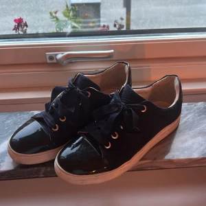 mörkblåa sneakers från Billi Bi i mocka - Snygga svarta sneakers från Billi Bi med ovandel i mocka och lackad tå. Skorna har breda svarta band som snörning och vit platt sula. Perfekta för dig som gillar en stilren men ändå unik look. Säljer pga att jag inte får användning av dem