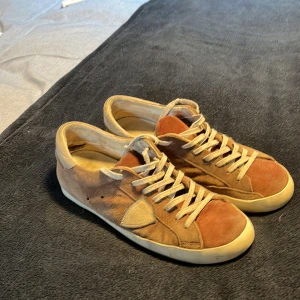 Philippe Model strl 42/43 - Snygga sneakers i mocka med bruna och beige toner. Skorna har rund tå, platt sula och klassisk snörning. Perfekta för dig som gillar en retrovibe och vill ha något som sticker ut lite men ändå är lättmatchat. Passar till både jeans och shorts. Är något slitna och låda tillkommer ej. Vid frågor tveka ej att hör av dig!!!!