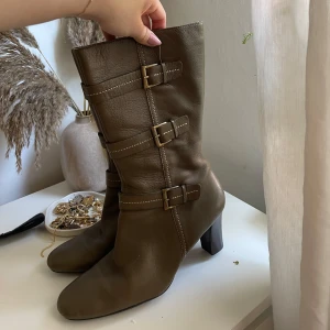 Olivgrön boots - Snygga olivgröna boots i skinn. Modellen har rund tå och stabil klack som ger lite höjd. Använt fåtal gånger, men fortfarande i bra skick.