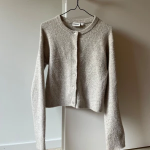 Beige kofta från Kappahl XS - Mysig beige kofta från Kappahl i storlek XS. Koftan har rund halsringning, långa ärmar och knäppning framtill med pärlemorknappar. Tillverkad i en mjuk blandning av polyester, akryl och ull för en skön känsla. 