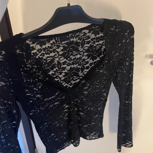 Svart spetsblus från Gina Tricot  - Supersnygg svart spetsblus från Gina Tricot i storlek XS. Blusen har lång ärm, v-ringning. Hela toppen är i genombruten spets med blommigt mönster, vilket ger en riktigt trendig och cool vibe.