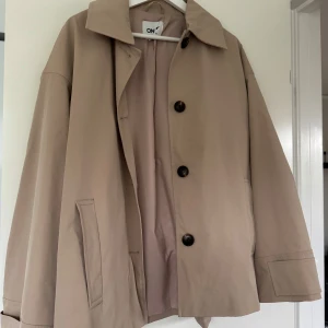 Beige rock från ONLY i storlek L - Stilren beige jacka från ONLY i storlek L. Jackan har klassisk krage, stora svarta knappar och raka fickor. 