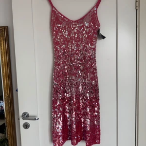 Rosa paljettklänning  - Vintage glittrig rosa kortklänning från pearce fionda med smala axelband och täckt av skimrande paljetter. Klänningen har en figurnära passform och är perfekt för dig som vill sticka ut. Materialet är mjukt och stretchigt för en bekväm känsla.
