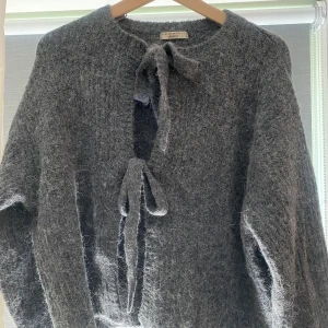 Grå stickad kofta med knyt från Ginatricot - Mysig grå stickad kofta från Ginatricot med två knytband framtill. Koftan har lång ärm och en fluffig, lite lurvig känsla